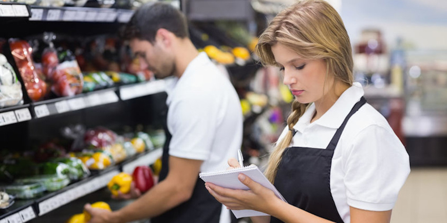 Serious staff woman wrting on notepad at supermarket
